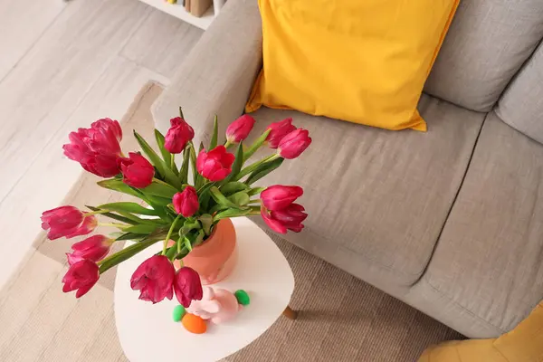 Vase with tulips, Easter rabbit and eggs on table in living room, top view