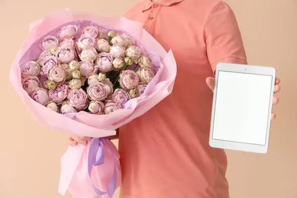 Male courier with bouquet of roses and tablet computer on beige background, closeup