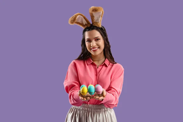 美丽的女人 长着兔子耳朵 背景是淡紫色的彩绘复活节彩蛋 — 图库照片