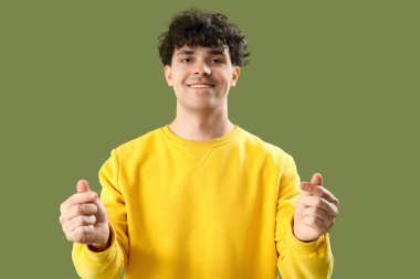 Yakışıklı genç adam yeşil arka planda parmaklarıyla kalp yapıyor.