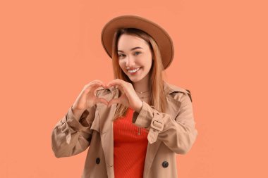 Elleri pembe arka planda kalp yapan genç bir kadın.