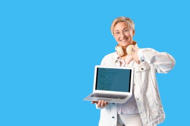 Mavi arka planda dizüstü bilgisayarı gösteren olgun bir kadın programcı.