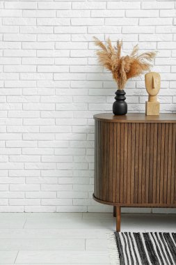Beyaz tuğla duvarın yanındaki dolapta biblo olan kurutulmuş pampa vazosu.