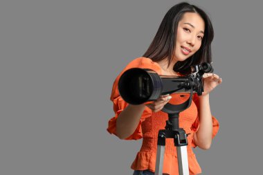 Genç Asyalı kadın gri arka planda teleskop kullanıyor.