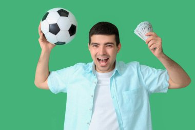 Futbol topu ve yeşil arka planda parası olan mutlu genç bir adam. Spor bahsi konsepti