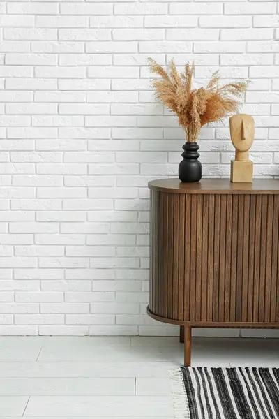 Beyaz tuğla duvarın yanındaki dolapta biblo olan kurutulmuş pampa vazosu.