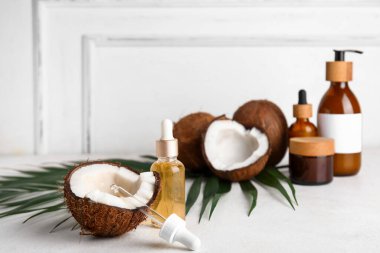 Tahta duvarın yanındaki beyaz masada farklı hindistan cevizi kozmetik yağı şişeleri var.