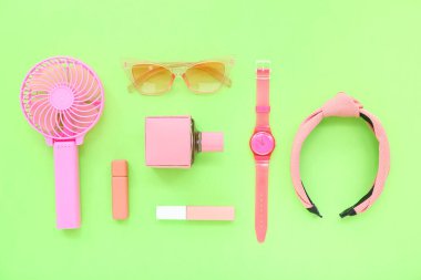 Pembe taşınabilir elektrikli vantilatör ve yeşil arka planda şık bayan aksesuarları olan kompozisyon