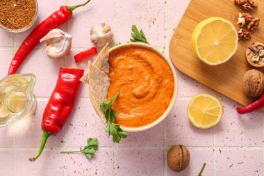 Bir kase lezzetli muhammara ve pembe fayanslı malzemeler.