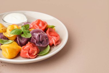 Bej arka planda fesleğen ve ekşi kremayla kaynamış renkli hamur köftesi tabağı.