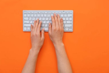 Turuncu arkaplana karşı bilgisayar klavyesinde yazan kadın elleri