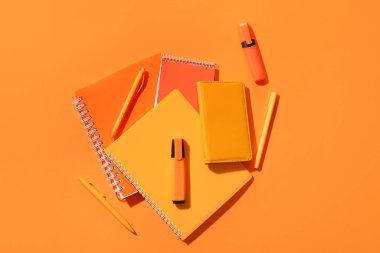 Turuncu arkaplan üzerine kalemler, kalemler ve defterler