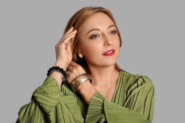 Gri arka planda şık aksesuarları olan güzel olgun bir kadın.