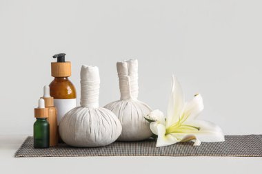 Güzel bir spa kompozisyonu, bitkisel poşetler, kozmetik ürünlerle dolu şişeler ve beyaz duvarın yanındaki masada çiçek.