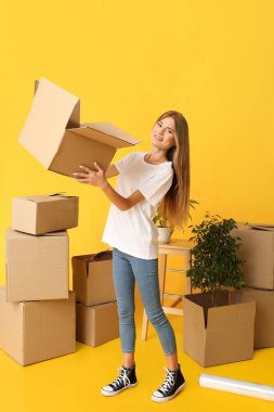 Sarı arka planda karton kutuları olan güzel bir genç kadın. Taşınma konsepti