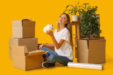Güzel genç bayan, sarı arka plandaki karton kutularda eşyalarını topluyor. Taşınma konsepti