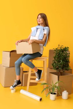 Sarı arka planda karton kutuları olan güzel bir genç kadın. Taşınma konsepti