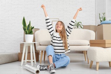 Yeni dairede karton kutularla otururken esnemekten yorgun düşmüş genç bir kadın.