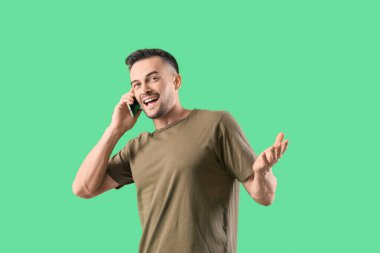 Yeşil arka planda cep telefonuyla konuşan mutlu genç adam.