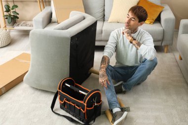 Düşünceli genç adam, evinde koltuk topluyor.