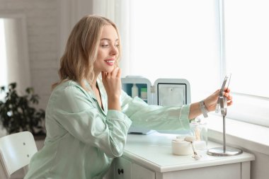 Kozmetik ürünleri için küçük buzdolabı olan güzel, mutlu bir kadın yatak odasında masada oturuyor.