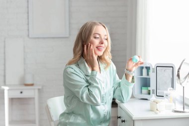 Kozmetik ürünleri için küçük buzdolabı olan, yatak odasına krem süren güzel, genç ve mutlu bir kadın.