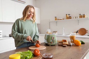 Genç ve güzel bir kadın mutfakta lezzetli sandviç yapmak için taze domates kesiyor.