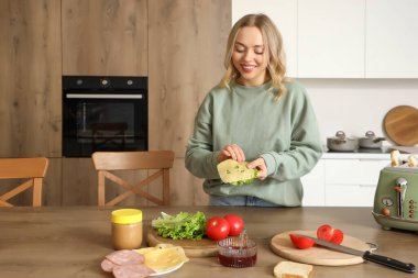 Genç ve güzel bir kadın mutfakta lezzetli bir sandviç yapıyor.