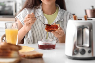 Genç ve güzel bir kadın portakal suyu içiyor ve reçelli tost yiyor.