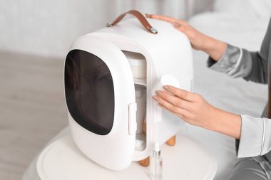 Kozmetik ürünleri için küçük buzdolabı olan güzel bir kadın yatak odasında oturuyor.