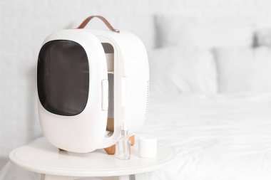 Yatak odasındaki masada kozmetik ürünleri için küçük bir buzdolabı.