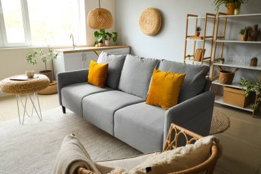 Işıl ışıl oturma odasının içinde rahat gri kanepe, sandalye, ev bitkileri ve hasır puflar