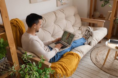 Bilgisayarlı yakışıklı adam modern oturma odasındaki beyaz koltukta dinlenirken görüntülü sohbet yapıyor.