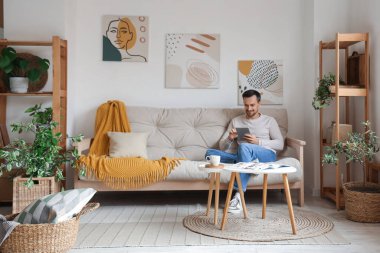 Modern oturma odasındaki beyaz koltukta dinlenen tablet bilgisayarlı yakışıklı adam.