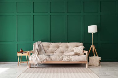 Yeşil duvarın yanında battaniyeli ve yastıklı rahat beyaz kanepe.