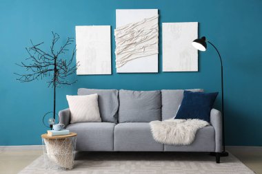 Rahat gri kanepe, yastıklar ve modern oturma odasındaki mavi duvarın yanında standart lamba.