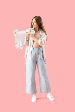 Pembe arka planda bebek tulumu giyen hamile bir kadın.