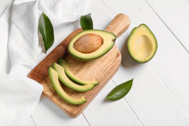 Taze avokadoların ve beyaz ahşap arka planda yaprakların olduğu tahta.