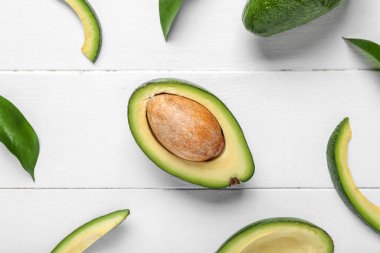 Taze olgun avokadolar ve beyaz ahşap arka planda yapraklar.