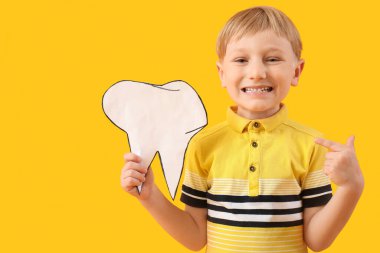 Sağlıklı dişleri olan küçük mutlu çocuk sarı arka plandaki kağıt dişlere bakıyor.