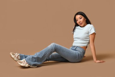 Kahverengi arka planda oturan şık kotlu güzel Asyalı kadın.