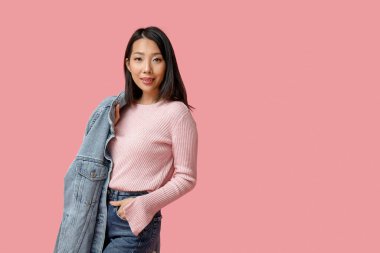 Pembe arka planda şık kot elbiseli güzel, mutlu Asyalı kadın.