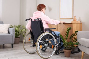 Tekerlekli sandalyedeki genç adam evdeki raftan dergi alıyor.