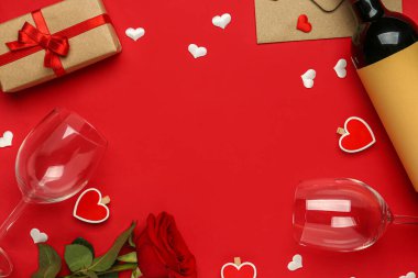 Kırmızı arka planda Sevgililer Günü için şarap, bardak, hediye kutusu ve gül çiçeğinden yapılmış bir çerçeve.