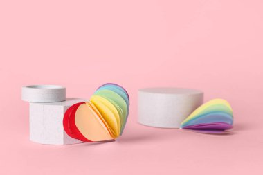Pembe arka planda LGBT bayrağı renginde kağıt kalpli dekoratif podyumlar. Sevgililer Günü kutlaması