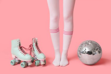 Pembe arka planda eski paten ve disko topu olan güzel genç bir kadın.