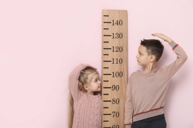 Sevimli küçük çocuklar pembe arka planda boy ölçüyorlar.