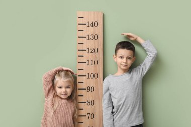 Sevimli küçük çocuklar yeşil arka planda boy ölçüyorlar.
