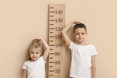 Bej arka planda boy ölçümü yapan sevimli küçük çocuklar.