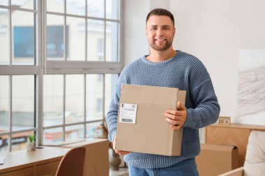 Evde paketleri açık genç bir adam var.